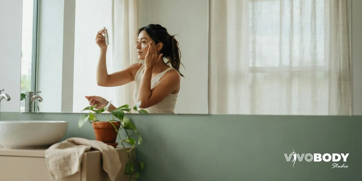Woman applying sunscreen to her cheek at a bathroom mirror